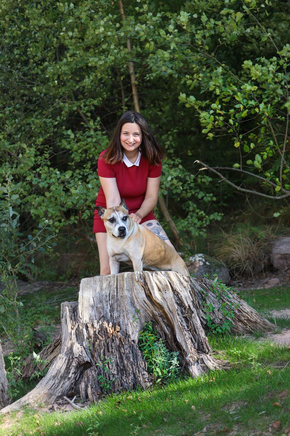 Charlène, souriante, avec sa chienne Joyce posée sur une souche en forêt
